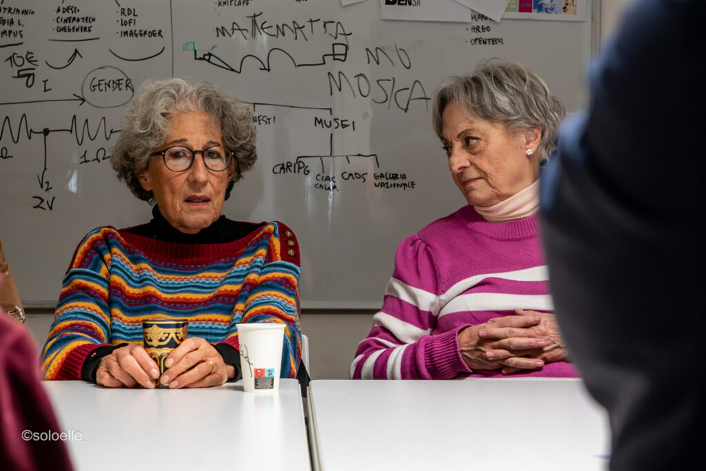 Due donne indossa maglioni colorati sedute al tavolo parlano
