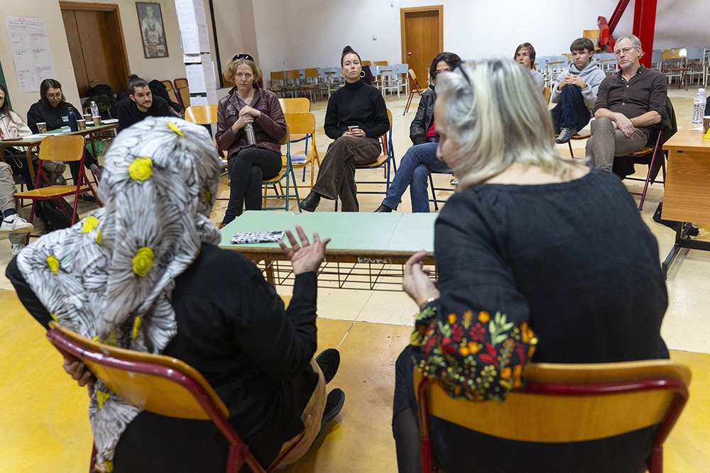 Due donne parlano al centro di un cerchio di persone sedute in cerchio, in un ambiente scolastico.